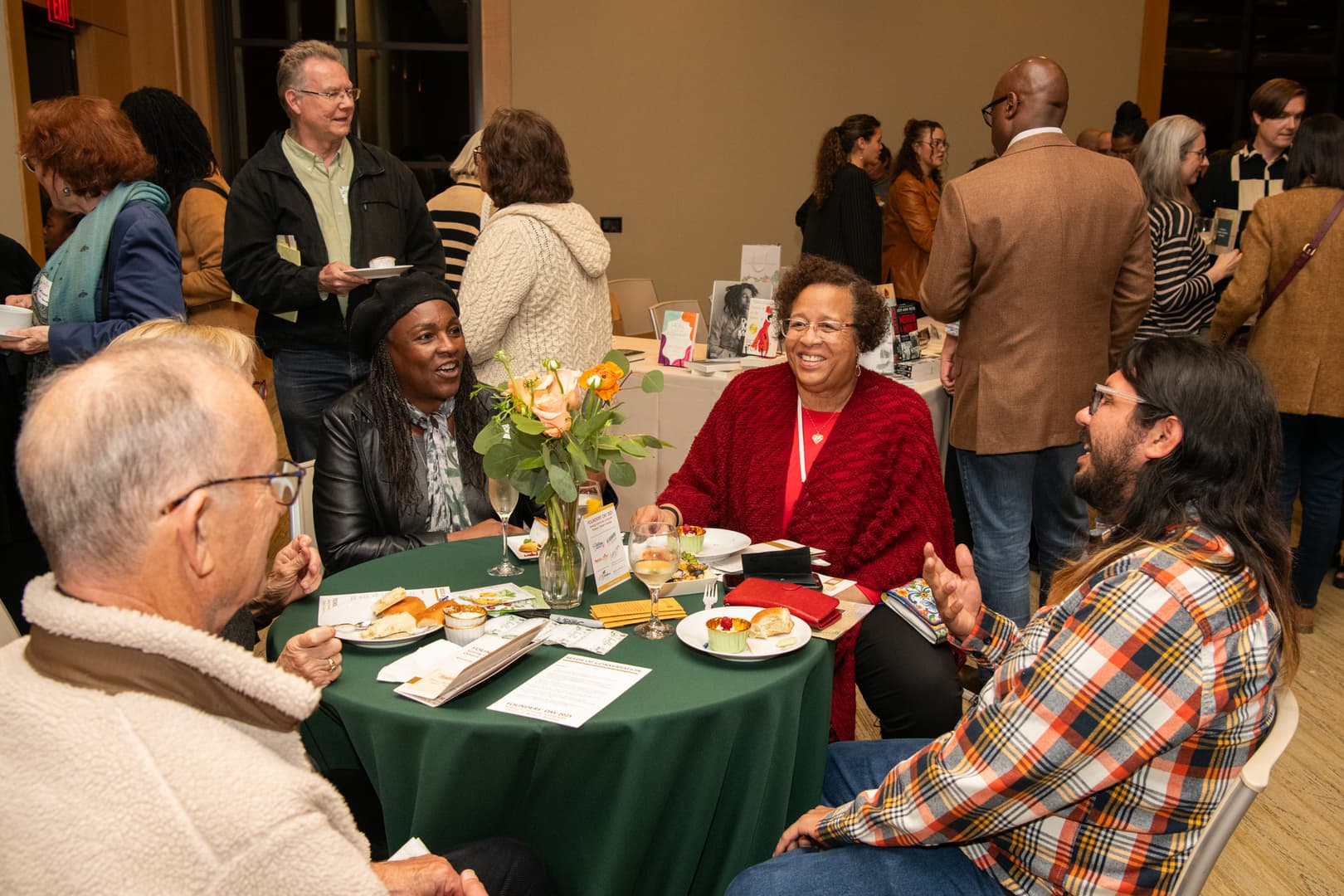 Four people sit at a table in a crowded room.
